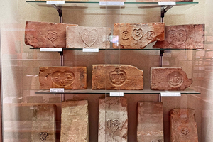  »Fig. 5: The heart was a very popular brick symbol that enjoyed widespread use and design creativity. The arrangement in the display case follows the probable development of the heart symbol from sketches of crossed plain tile moulds (bottom left) to the pretzel shape and finally to decorative hearts 