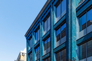  » The bricks at the building’s base are colored dark blue, while further up the facade the color changes into lighter shades of blue and green 