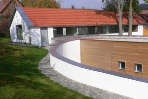  &gt;&gt; Passivhaus in Essenbach: Die ehemalige Hofstelle liegt an einem Hang und wird teilweise von einer im Bogen verlaufenden Mauer umfasst. 